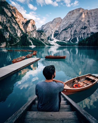 一个男人坐在棕色的木楼梯上，白天凝视着山附近的湖面